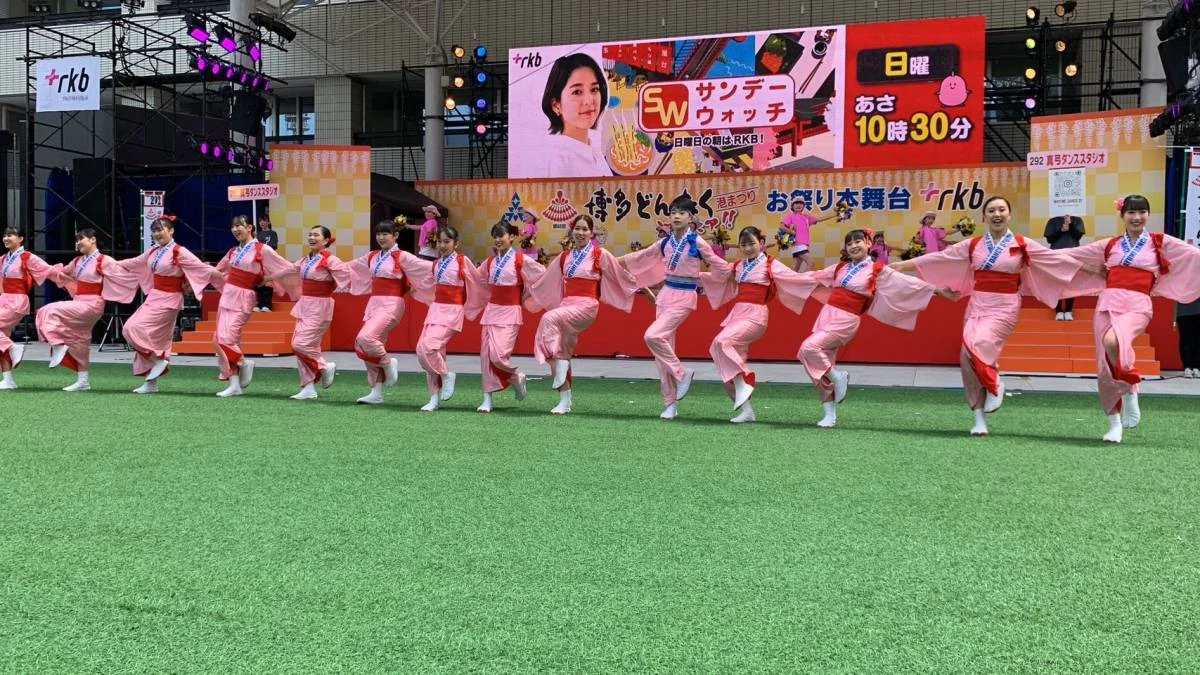屋外舞台でピンクの衣装を着て踊る出演者たち